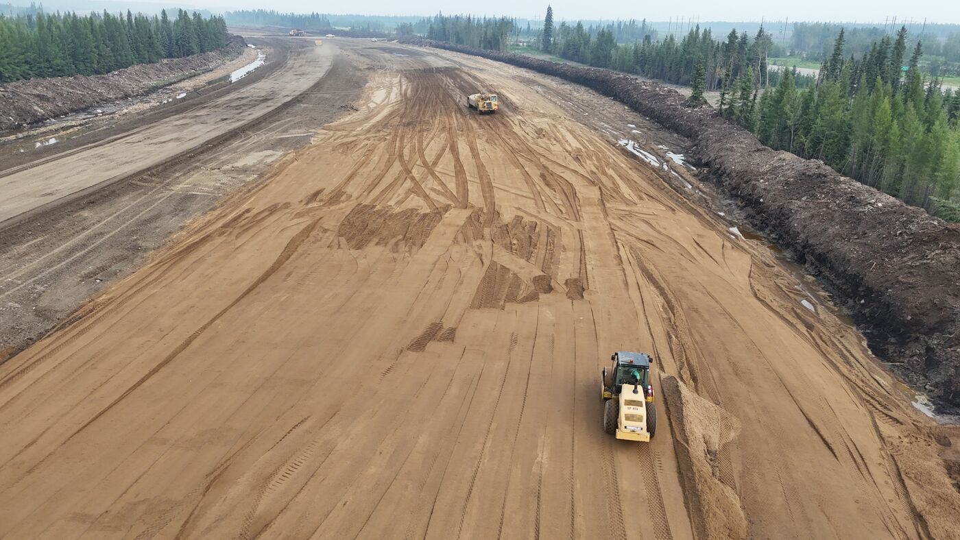 Aerial view of a graded highway corridor with a compactor working the surface